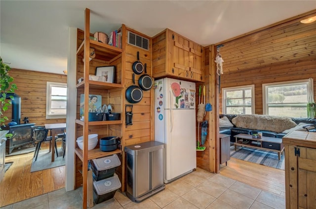 kitchen with plenty of natural light, freestanding refrigerator, wooden walls, and a wood stove