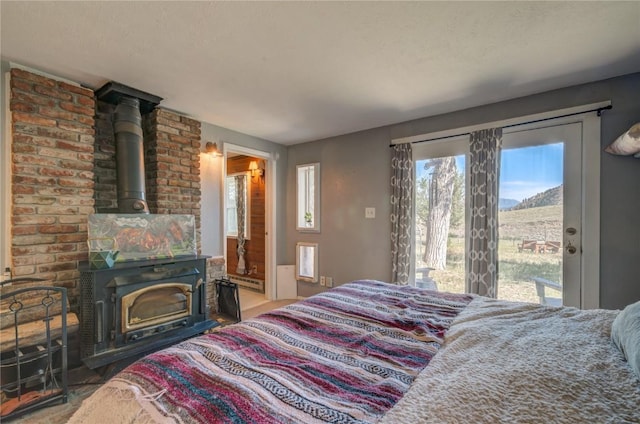 bedroom with a baseboard radiator, a wood stove, and access to outside