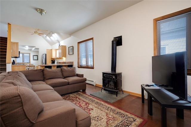 living room featuring vaulted ceiling, a wood stove, a baseboard radiator, plenty of natural light, and ceiling fan