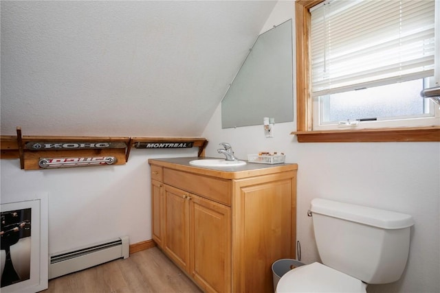 bathroom with lofted ceiling, hardwood / wood-style flooring, baseboard heating, vanity, and toilet