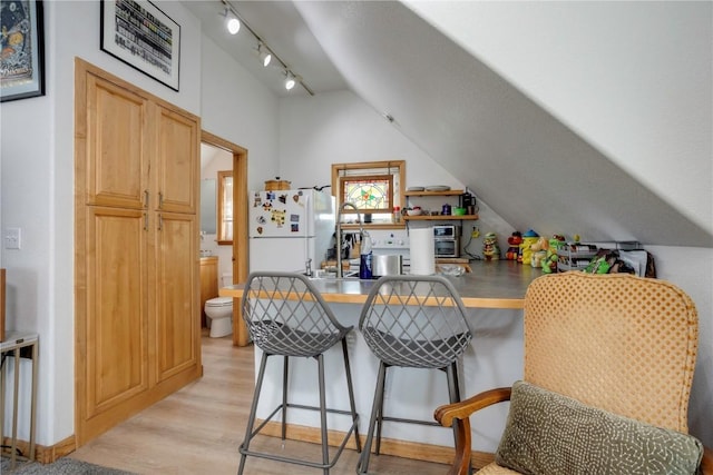 kitchen featuring lofted ceiling, a kitchen breakfast bar, white refrigerator, kitchen peninsula, and light wood-type flooring