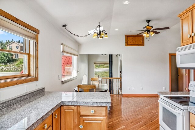 kitchen featuring kitchen peninsula, light hardwood / wood-style floors, lofted ceiling, white appliances, and ceiling fan with notable chandelier