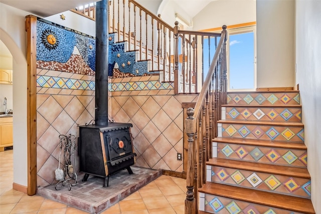 staircase featuring a wood stove, tile patterned flooring, lofted ceiling, and sink