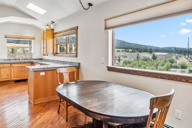 kitchen featuring a mountain view, lofted ceiling with skylight, decorative backsplash, light hardwood / wood-style floors, and kitchen peninsula