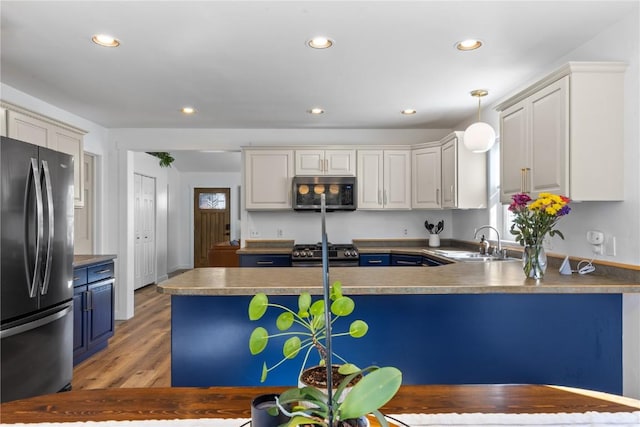 kitchen with sink, gas stove, white cabinetry, stainless steel fridge, and pendant lighting