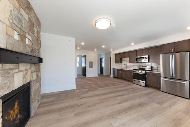 kitchen featuring light wood finished floors, stainless steel appliances, a stone fireplace, dark brown cabinetry, and decorative backsplash