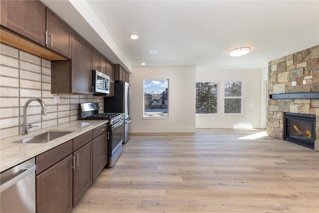 kitchen with a sink, open floor plan, stainless steel appliances, a stone fireplace, and decorative backsplash