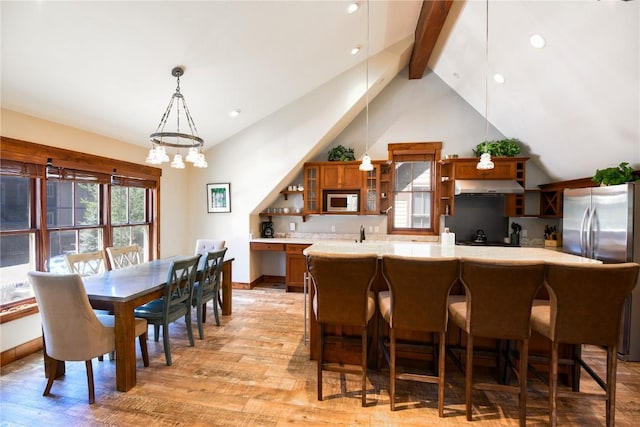 kitchen featuring lofted ceiling with beams, kitchen peninsula, stainless steel fridge, decorative light fixtures, and light wood-type flooring