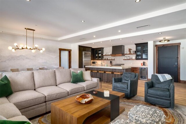 kitchen featuring stainless steel built in fridge, wall chimney range hood, tasteful backsplash, a kitchen island with sink, and a kitchen breakfast bar