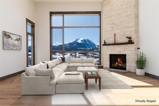 living area featuring wood finished floors, baseboards, a fireplace, a towering ceiling, and a mountain view