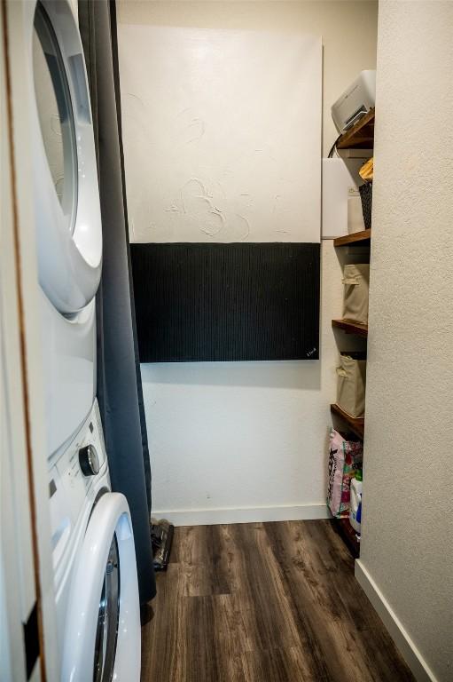 clothes washing area with dark hardwood / wood-style flooring and stacked washer / drying machine