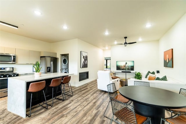 kitchen featuring ceiling fan, stainless steel appliances, a kitchen breakfast bar, light hardwood / wood-style flooring, and stacked washer and dryer