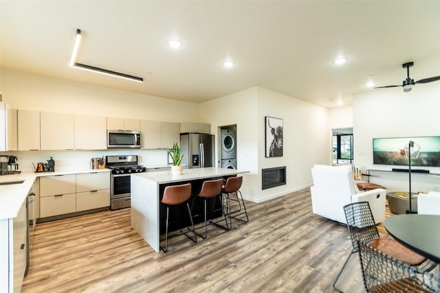 kitchen with ceiling fan, a center island, light hardwood / wood-style floors, stacked washer and clothes dryer, and appliances with stainless steel finishes