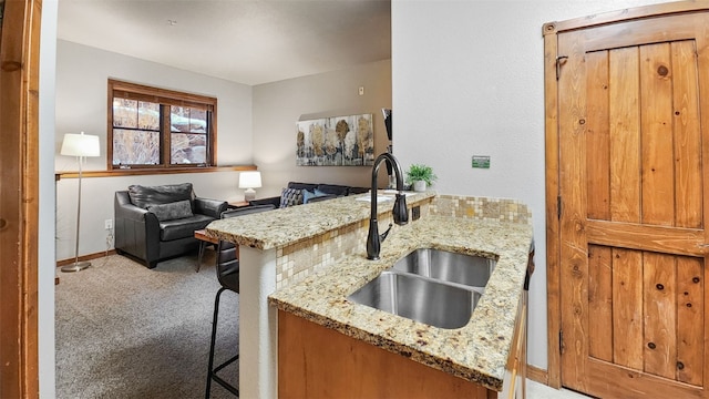 kitchen with a breakfast bar, sink, kitchen peninsula, carpet floors, and light stone countertops