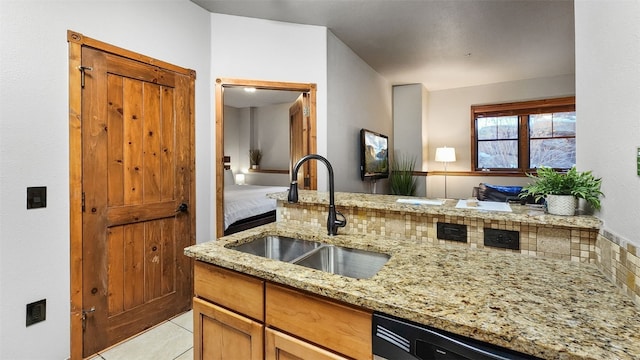 kitchen featuring light tile patterned flooring, black dishwasher, sink, and light stone counters