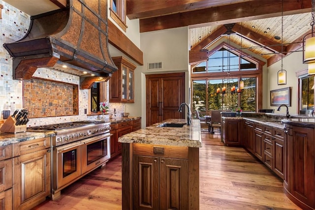 kitchen featuring a center island with sink, range with two ovens, sink, tasteful backsplash, and beamed ceiling