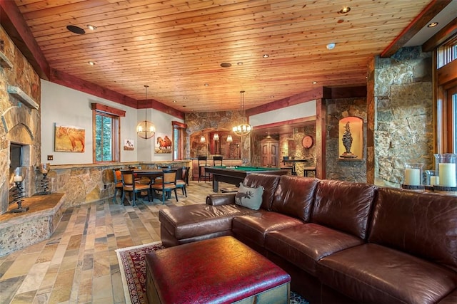 living room featuring a stone fireplace, billiards, wooden ceiling, and an inviting chandelier