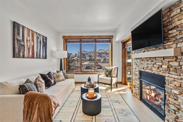 living room featuring baseboards, a stone fireplace, and light wood finished floors