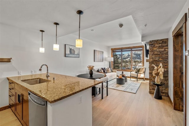 kitchen featuring light stone counters, light wood finished floors, stainless steel dishwasher, open floor plan, and a sink