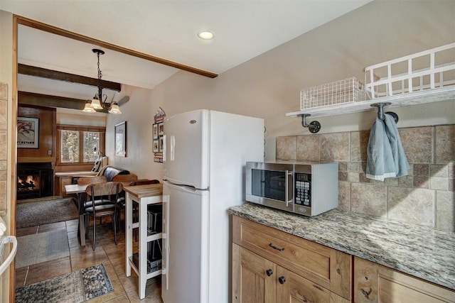 kitchen featuring beam ceiling, stainless steel microwave, hanging light fixtures, freestanding refrigerator, and a lit fireplace