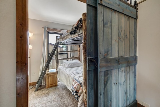 carpeted bedroom featuring a barn door and baseboards