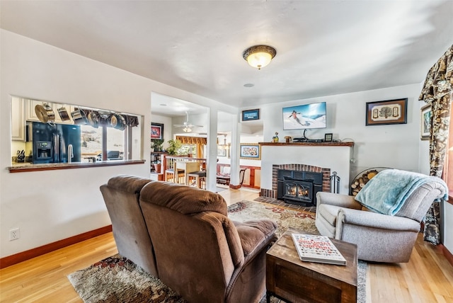 living room with light hardwood / wood-style floors, a brick fireplace, and ceiling fan