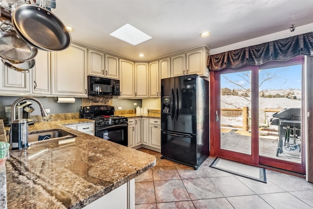 kitchen featuring a skylight, sink, black appliances, stone countertops, and cream cabinetry