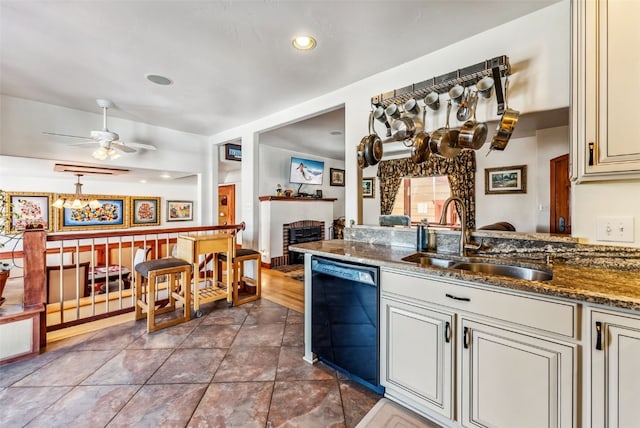 kitchen featuring ceiling fan, dishwasher, sink, a brick fireplace, and dark stone countertops