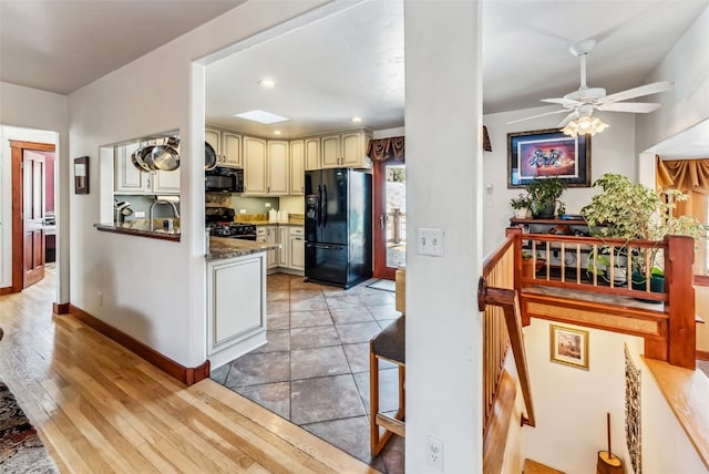 kitchen with ceiling fan, sink, black appliances, light hardwood / wood-style flooring, and dark stone countertops