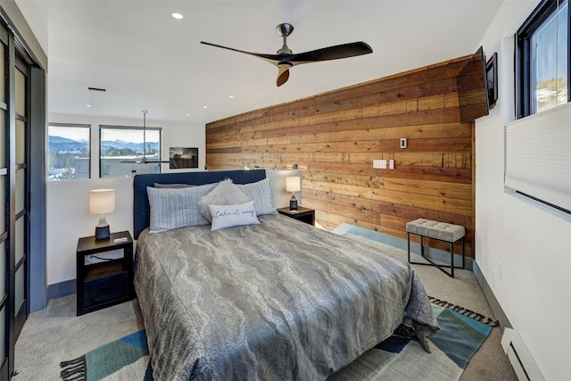 carpeted bedroom featuring ceiling fan, wooden walls, and a baseboard heating unit