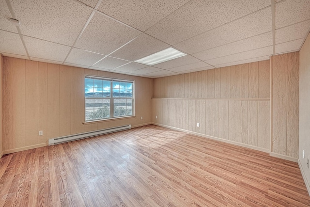 unfurnished room featuring a baseboard radiator, a paneled ceiling, baseboards, and wood finished floors