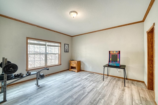 workout area with ornamental molding, baseboards, and light wood finished floors