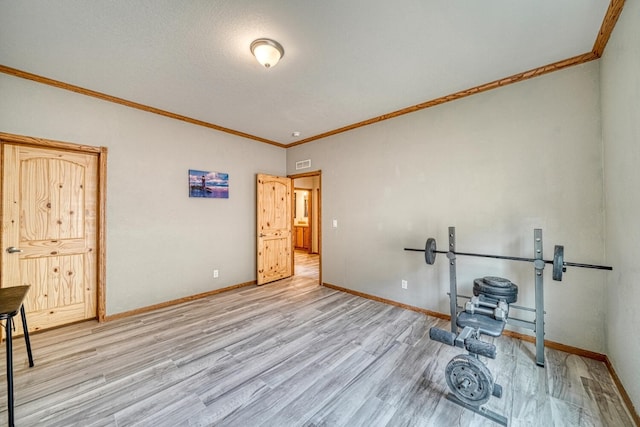 workout room featuring baseboards, light wood-type flooring, and crown molding