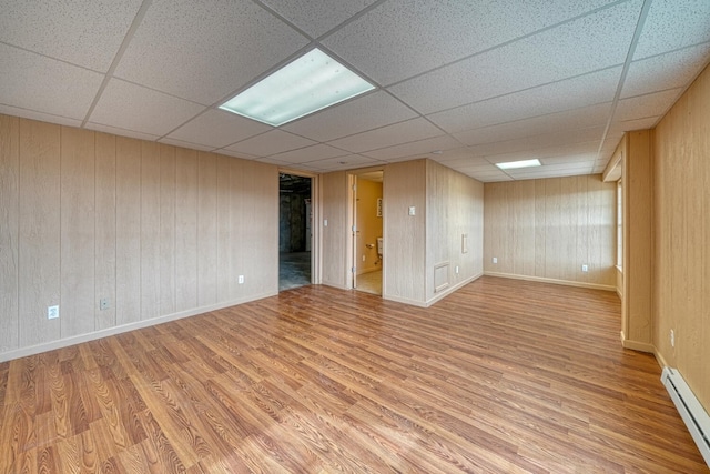 finished basement featuring baseboards, a baseboard heating unit, a drop ceiling, and wood finished floors