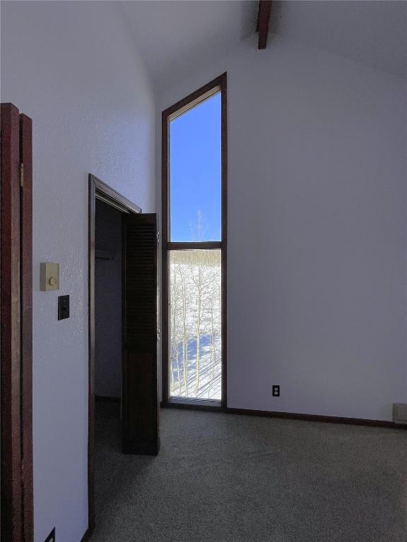 carpeted spare room featuring vaulted ceiling with beams