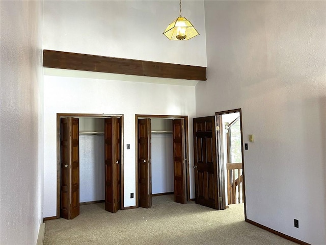 unfurnished bedroom featuring a towering ceiling, light colored carpet, and multiple closets