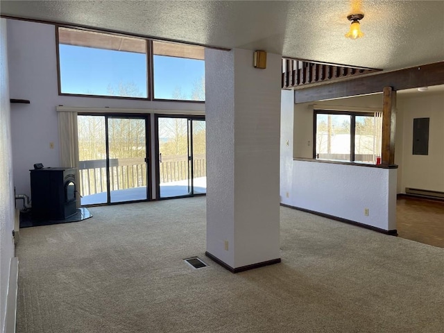 unfurnished living room featuring carpet, a wood stove, a textured ceiling, and electric panel