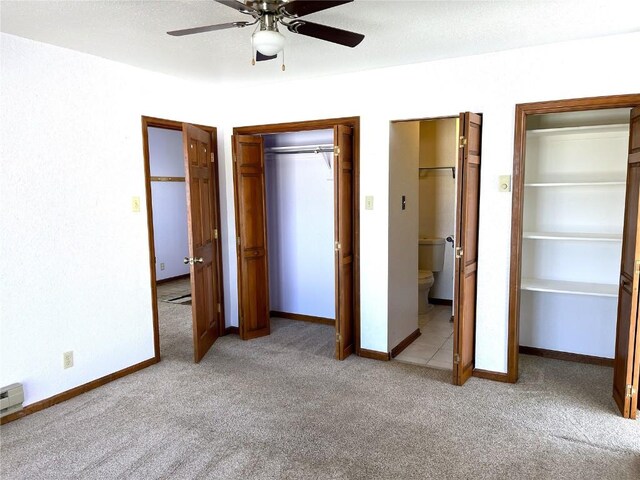 unfurnished bedroom featuring ceiling fan, light colored carpet, multiple closets, and ensuite bath