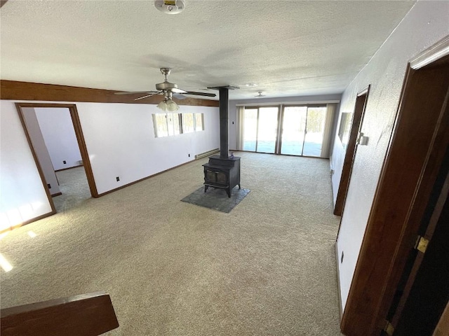 unfurnished living room featuring a wood stove, light carpet, ceiling fan, and a textured ceiling