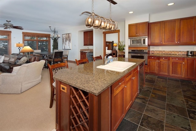 kitchen featuring a center island with sink, appliances with stainless steel finishes, light stone countertops, pendant lighting, and sink