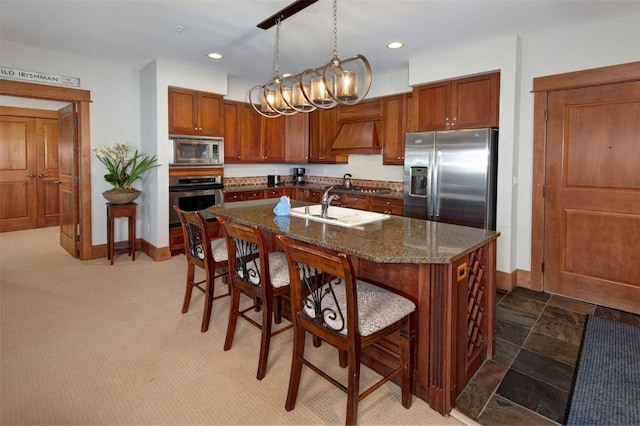 kitchen featuring decorative light fixtures, a kitchen island with sink, dark stone counters, appliances with stainless steel finishes, and a kitchen breakfast bar