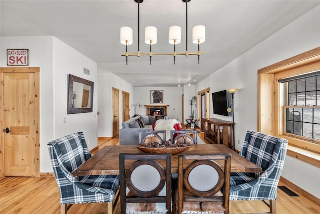 dining area with light wood finished floors, a brick fireplace, visible vents, and baseboards