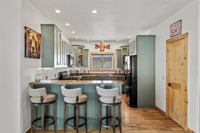 kitchen with a peninsula, a sink, green cabinets, freestanding refrigerator, and gas range