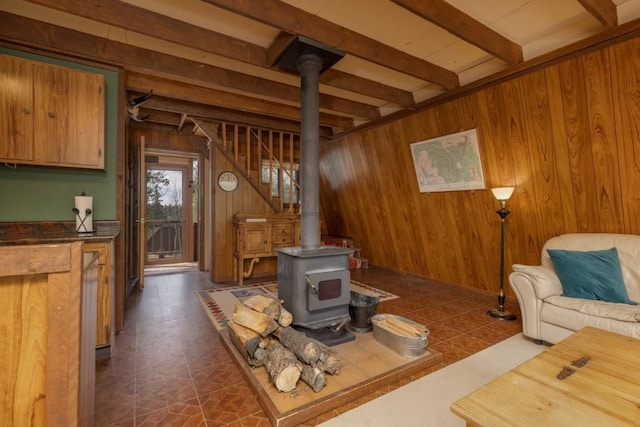 living room featuring beam ceiling, a wood stove, dark tile patterned floors, and wooden walls