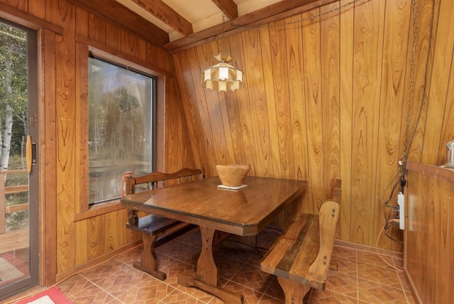 dining area featuring beamed ceiling and wood walls