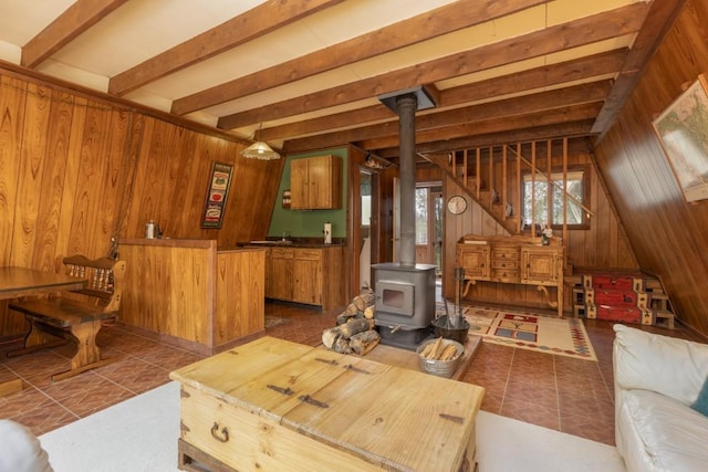 living room featuring beam ceiling, a wood stove, wooden walls, and tile patterned flooring