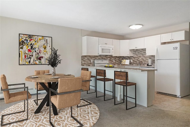 kitchen featuring white appliances, white cabinets, light tile patterned floors, a kitchen bar, and kitchen peninsula