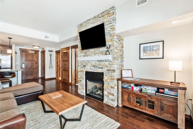 living room featuring visible vents, dark wood-style flooring, and a stone fireplace