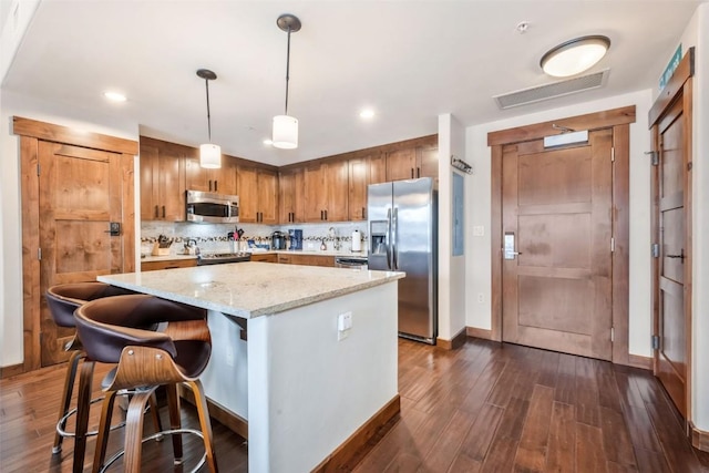 kitchen with visible vents, a kitchen island, brown cabinets, stainless steel appliances, and pendant lighting