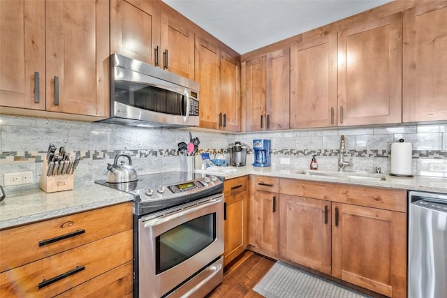 kitchen featuring tasteful backsplash, dark wood-style floors, light stone counters, stainless steel appliances, and a sink